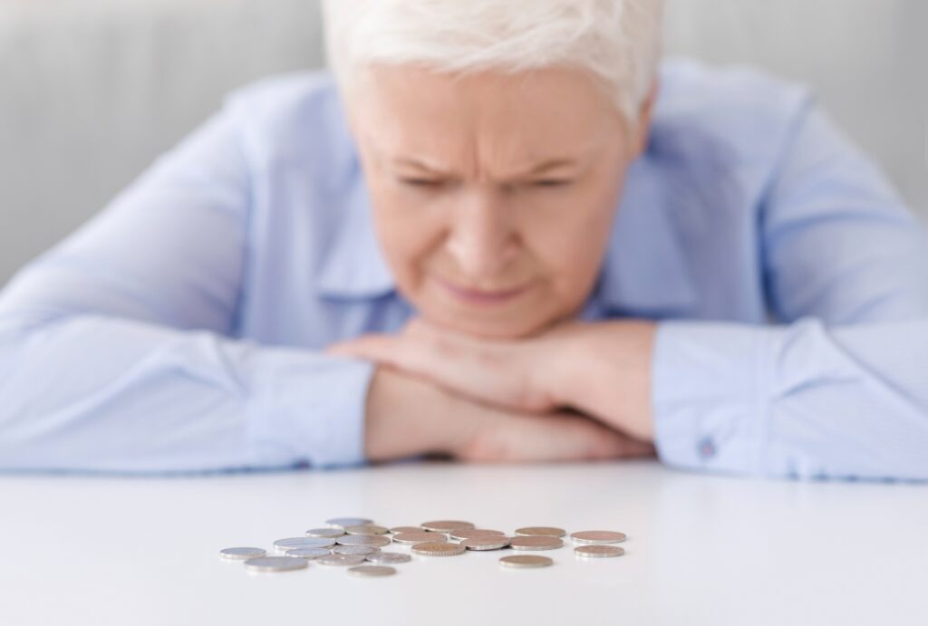 Elderly Poverty. Depressed senior woman looking at last coins lying at table, counting remaining money, suffering from poorness, selective focus