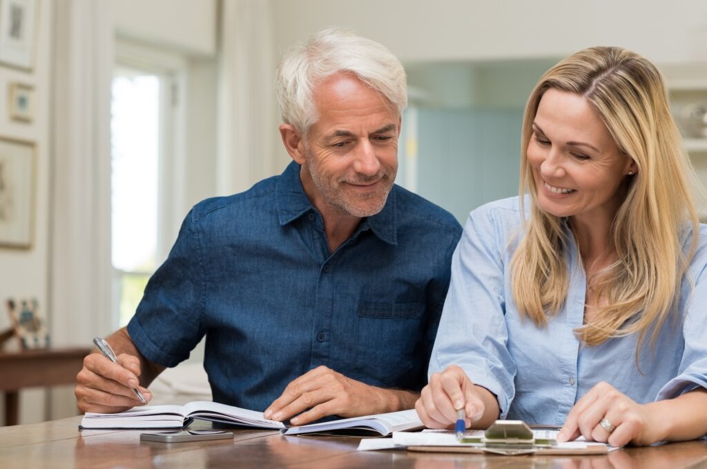 Mature couple doing family finances at home. Senior couple discussing home economics sitting at table. Happy couple sitting at home planning household financials.
