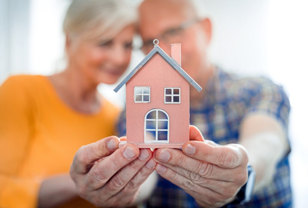 New house concept, happy senior couple holding small home model