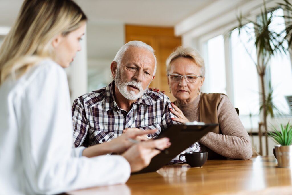 Mature couple looking at their plan of care and medications with female nurse at home.