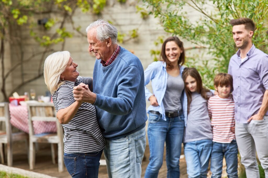 Happy grandparents dance waltz in front of family at a celebration in the garden